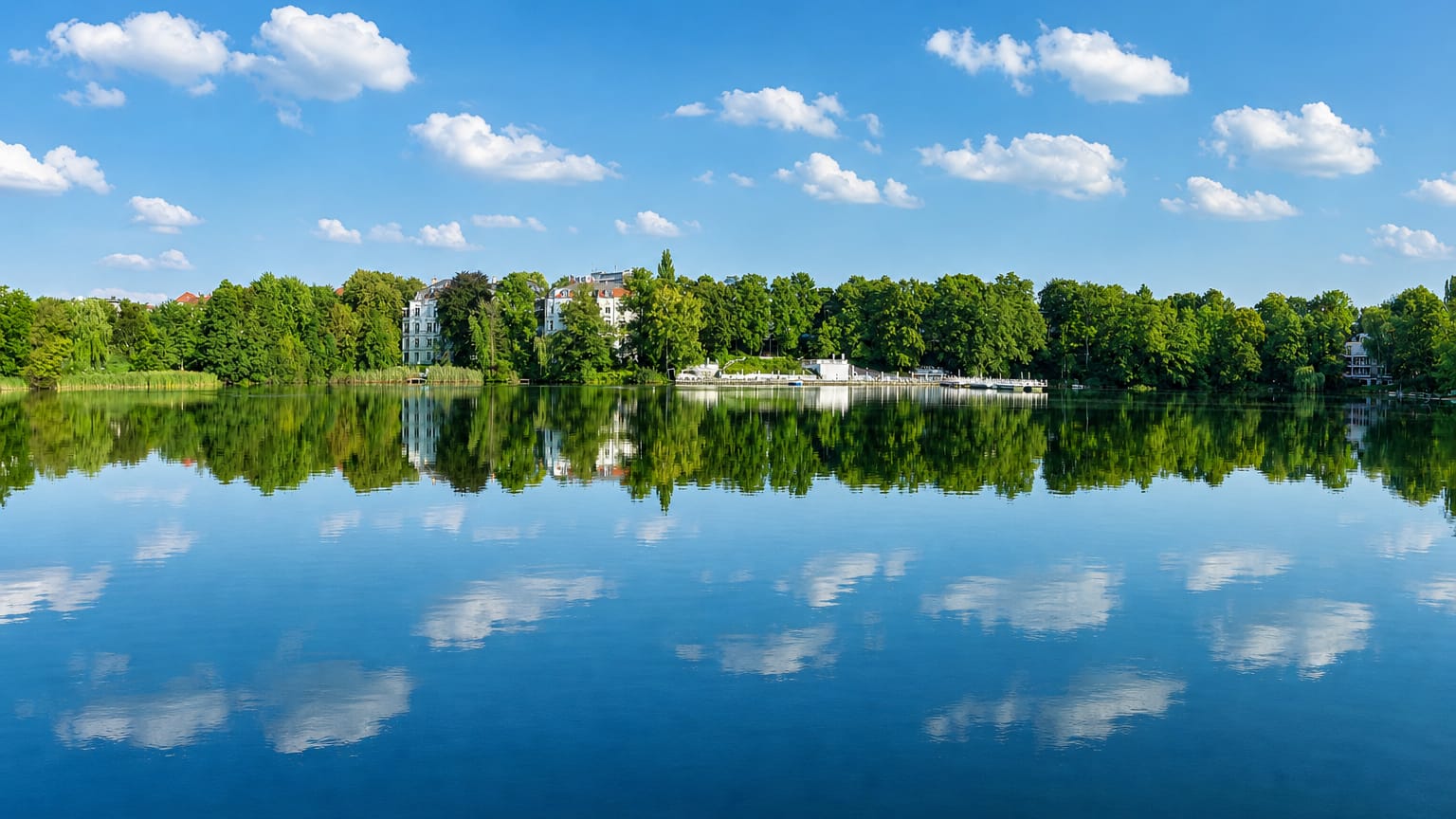 The Halensee lake in Berlin with a tree-lined shore and villas mirrored in calm blue water.