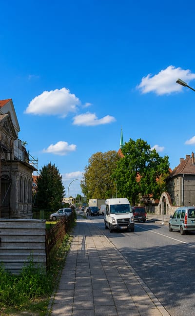 Residential street with old plastered houses, parked cars and a distant church spire in Heinersdorf, Berlin