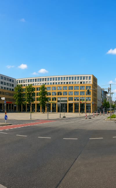 Wide tram-lined boulevard junction flanked by mid-rise commercial buildings in Hellersdorf, Berlin
