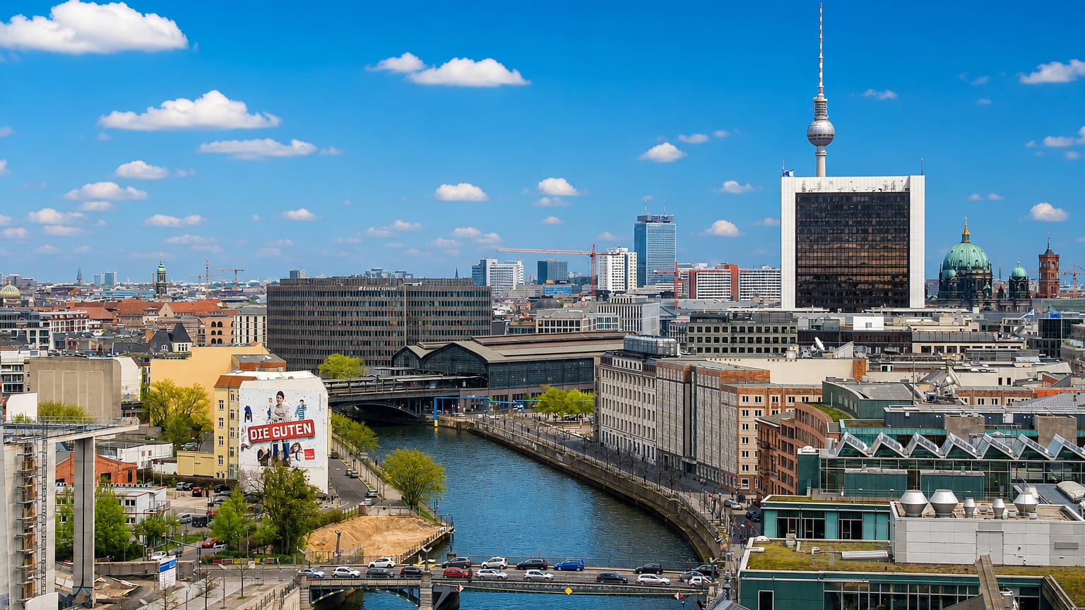 Berlin cityscape along the Spree with the Fernsehturm TV tower and the Berliner Dom cupola under a blue sky.