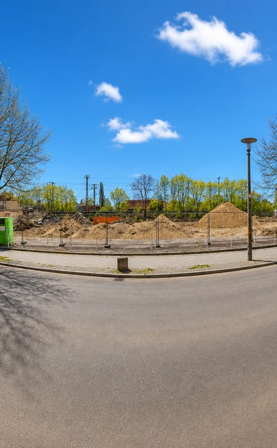 Wide street-corner view of older apartment blocks and a cleared lot in Karlshorst, Berlin, in early spring