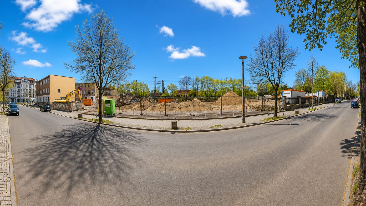 Wide street-corner view of older apartment blocks and a cleared lot in Karlshorst, Berlin, in early spring