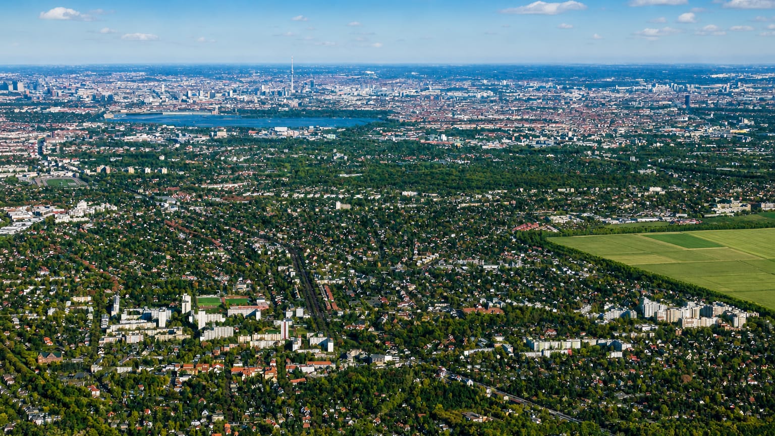 Aerial view over the leafy low-rise suburb of Lichtenrade, Berlin, with a lake and the distant city skyline.