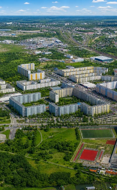 Aerial view of Neu-Hohenschonhausen in Berlin with colourful prefab panel housing blocks, a sports field and greenery
