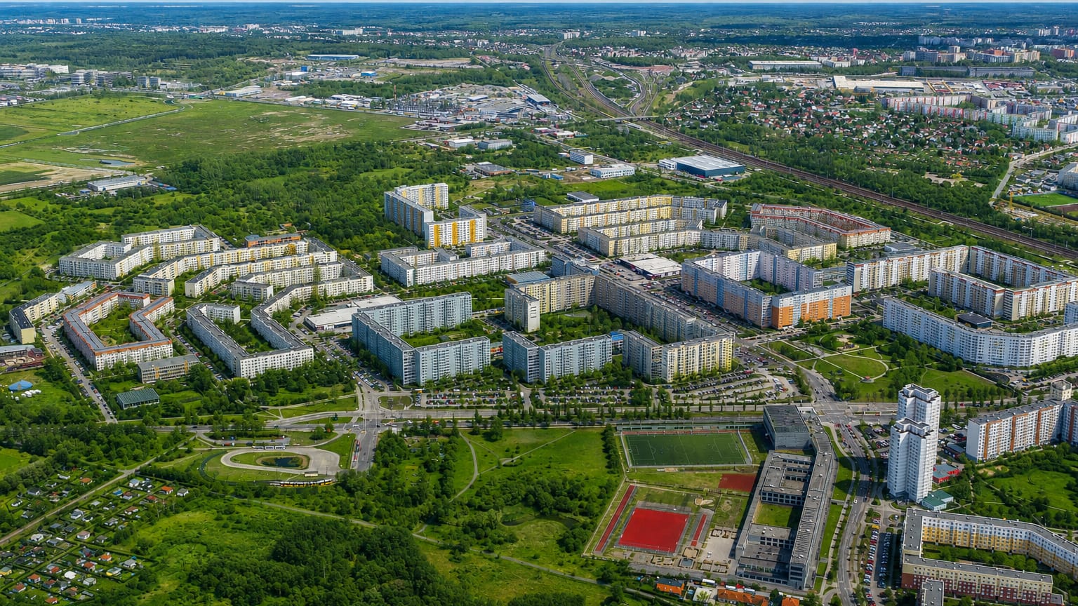 Aerial view of Neu-Hohenschonhausen in Berlin with colourful prefab panel housing blocks, a sports field and greenery