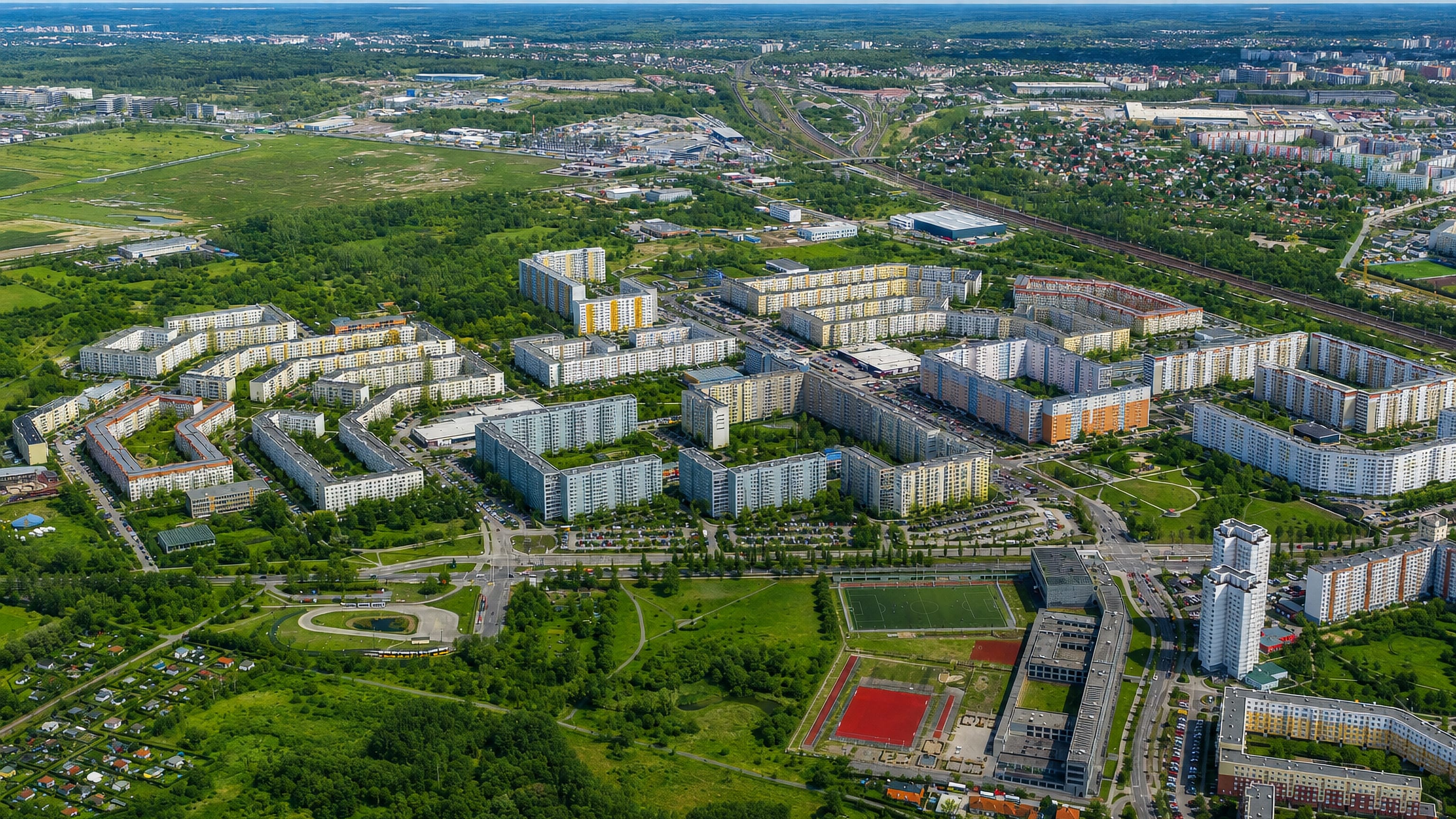 Aerial view of Neu-Hohenschonhausen in Berlin with colourful prefab panel housing blocks, a sports field and greenery