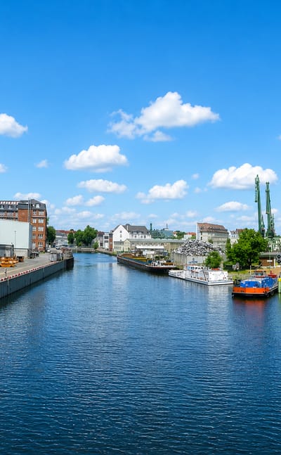 Industrial canal in Neukölln, Berlin, with grain silos, moored barges and a work boat under a bright sky.