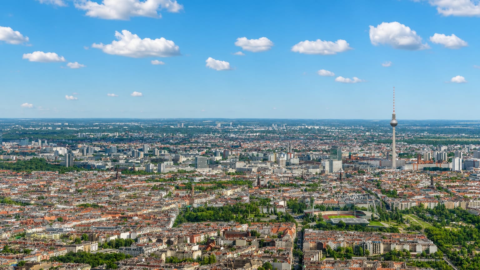Wide aerial of Prenzlauer Berg's dense old tenement rooftops with the Berlin TV Tower rising on the skyline.