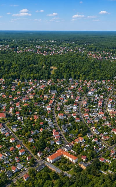 Aerial of Rahnsdorf in Berlin, a leafy villa settlement beside a forest and lakeshore with a curving rail line