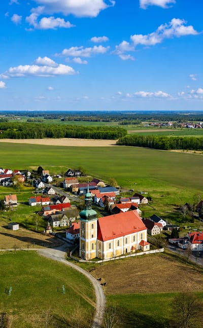 Aerial of a village with a baroque green-domed church amid open fields, evoking Rosenthal, Berlin