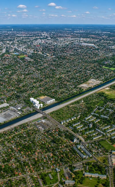 High aerial of Rudow in Berlin showing a straight canal cutting through suburban housing and greenery toward the hazy city