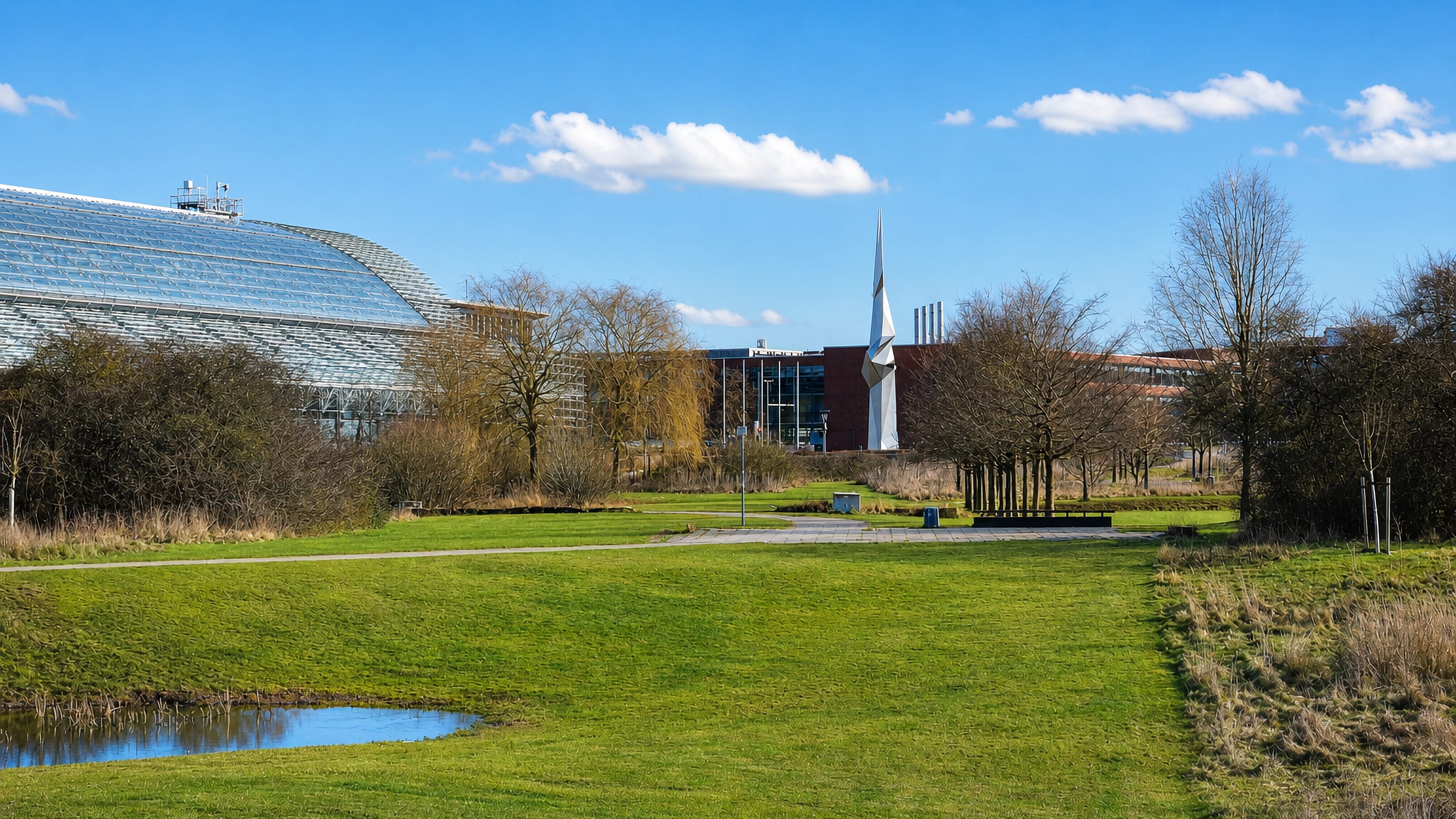Parkland and pond in front of the curved glass exhibition hall and sail sculpture at Bemerode, Hannover