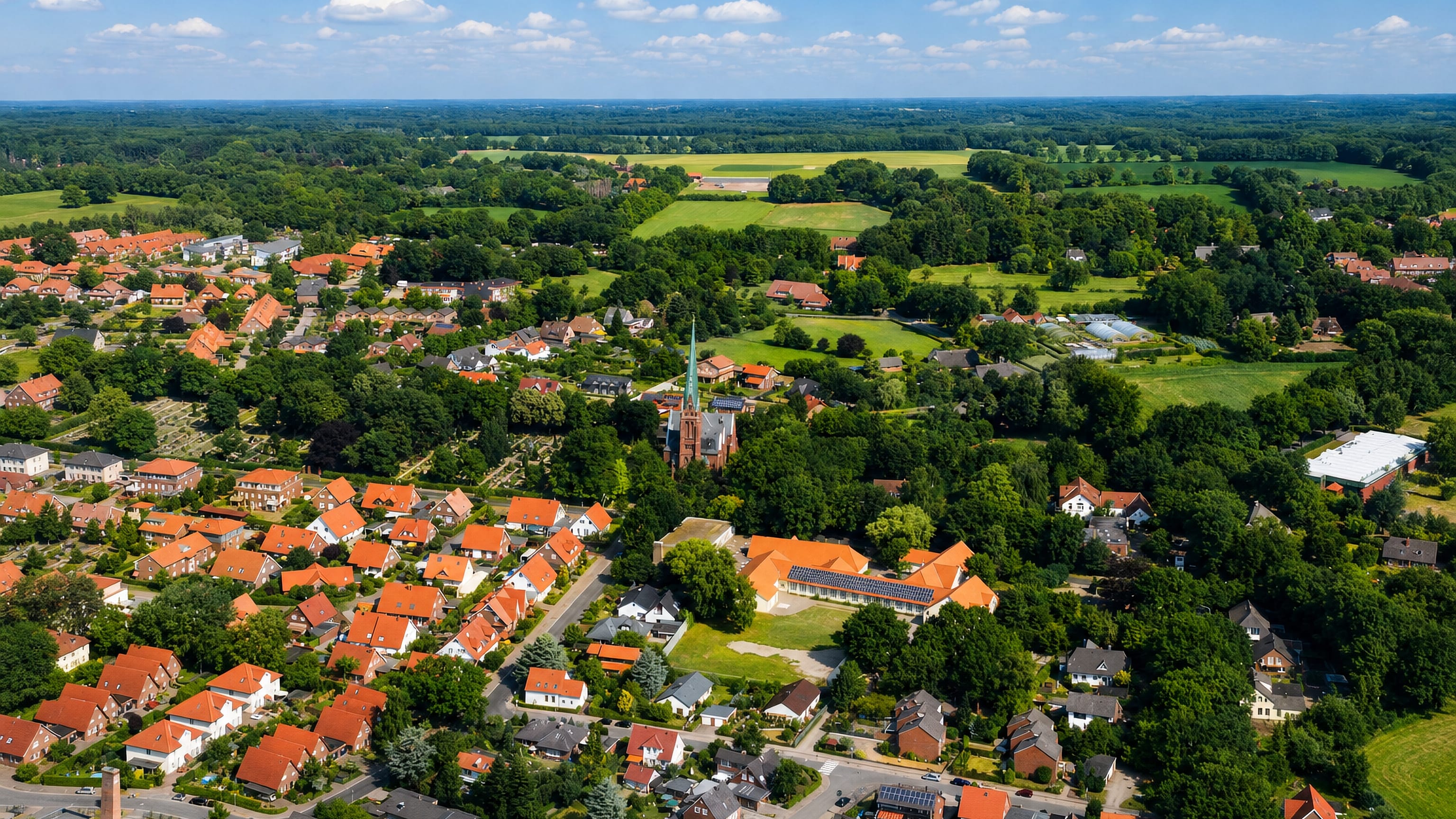 Ohmstede in Oldenburg from the air, red-tiled roofs around a brick church spire with farmland beyond