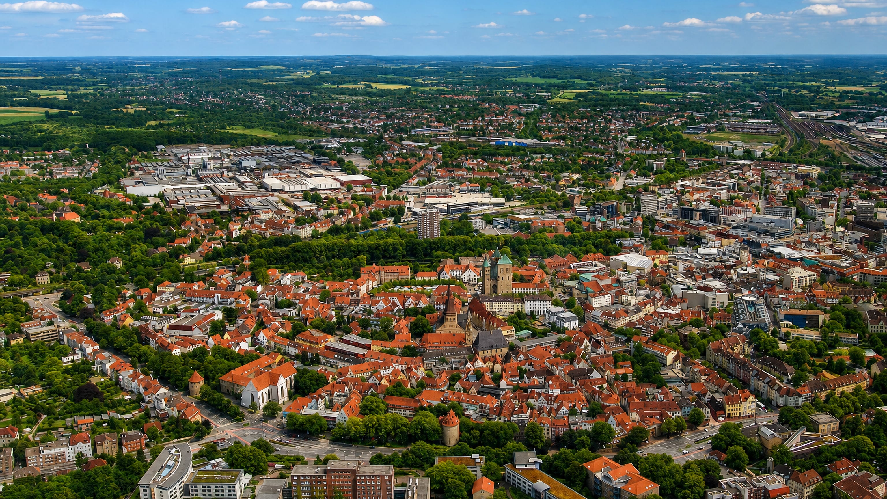 Aerial view over Osnabrück's red-roofed old town, cathedral towers and the surrounding green countryside
