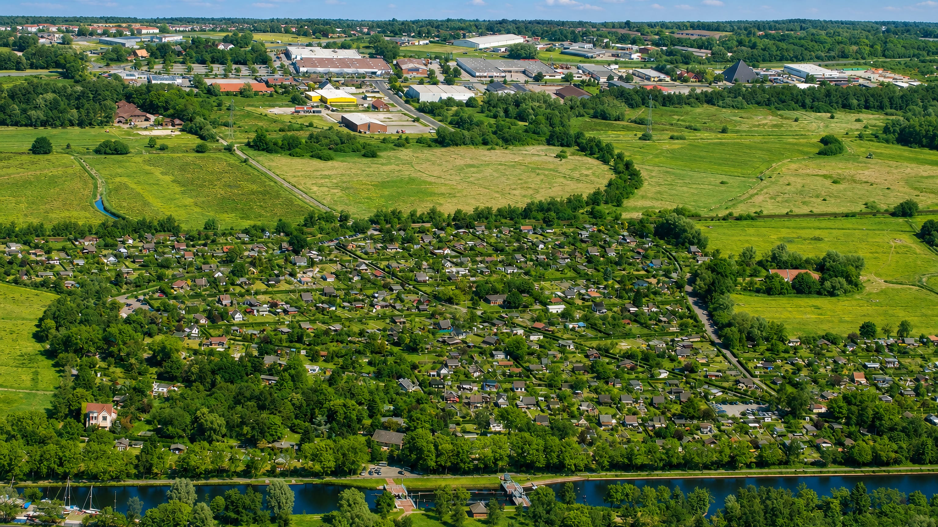 Aerial view over Ebkeriege in Wilhelmshaven, with allotment gardens, meadows and a canal below an industrial estate.