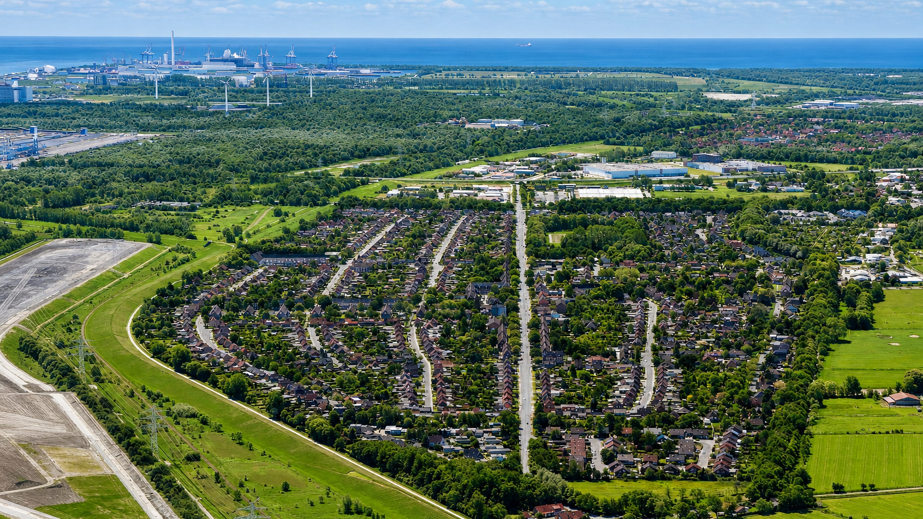 Aerial view of Voslapp, Wilhelmshaven, its green suburban streets reaching to the Jade Bay coast and port cranes.