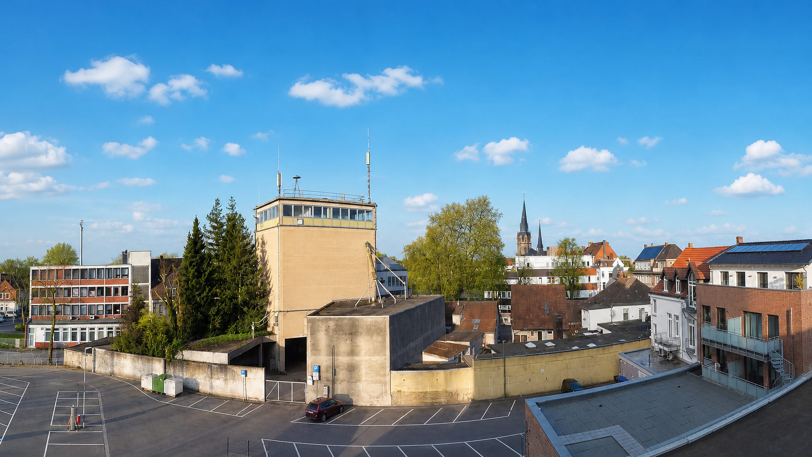 Ahlen in Westphalia, rooftops and church spires rising beyond a blocky tower and an empty car park
