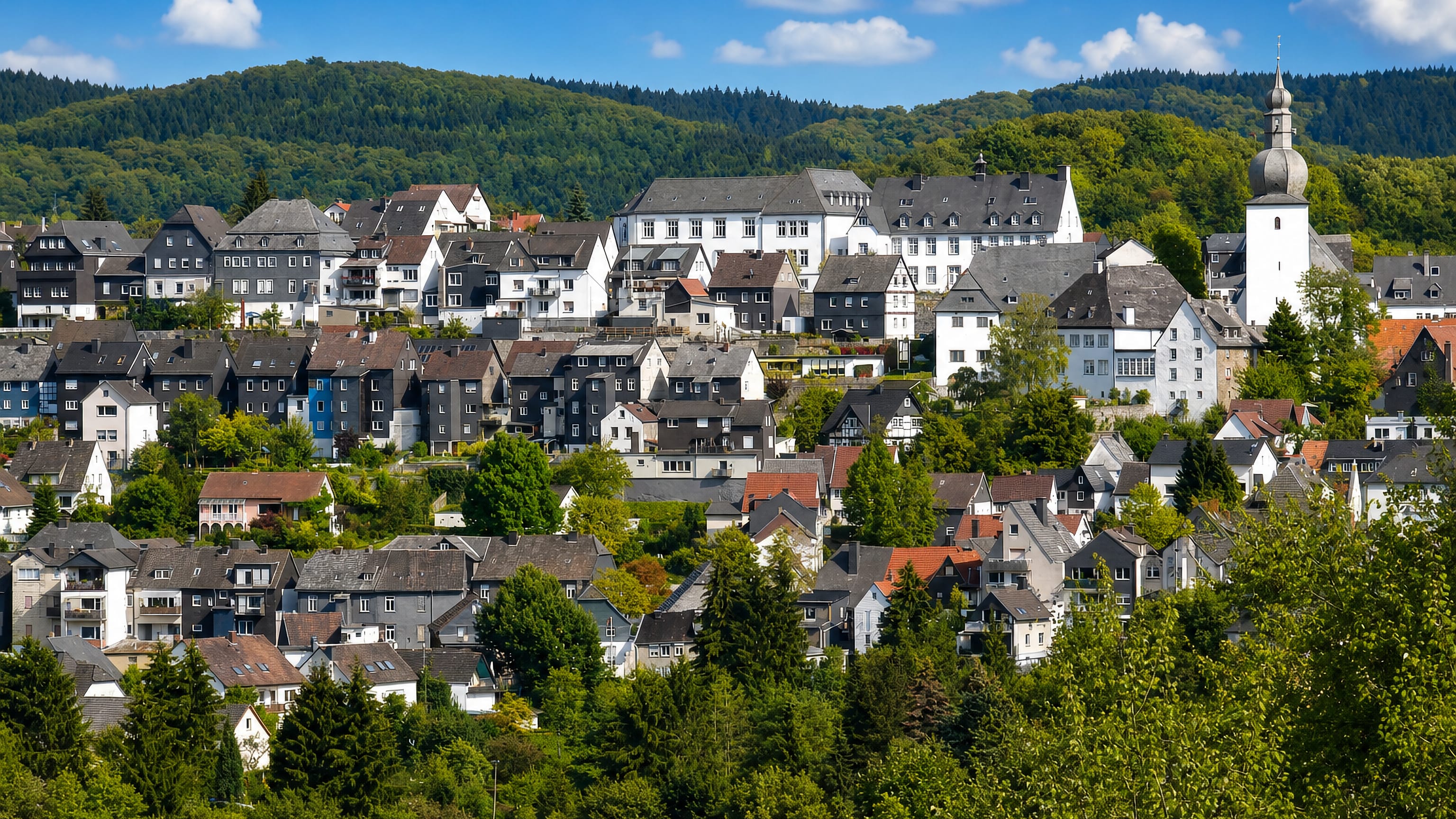 Slate-roofed houses and a baroque church spire on the wooded hillside of Arnsberg in Germany's Sauerland.