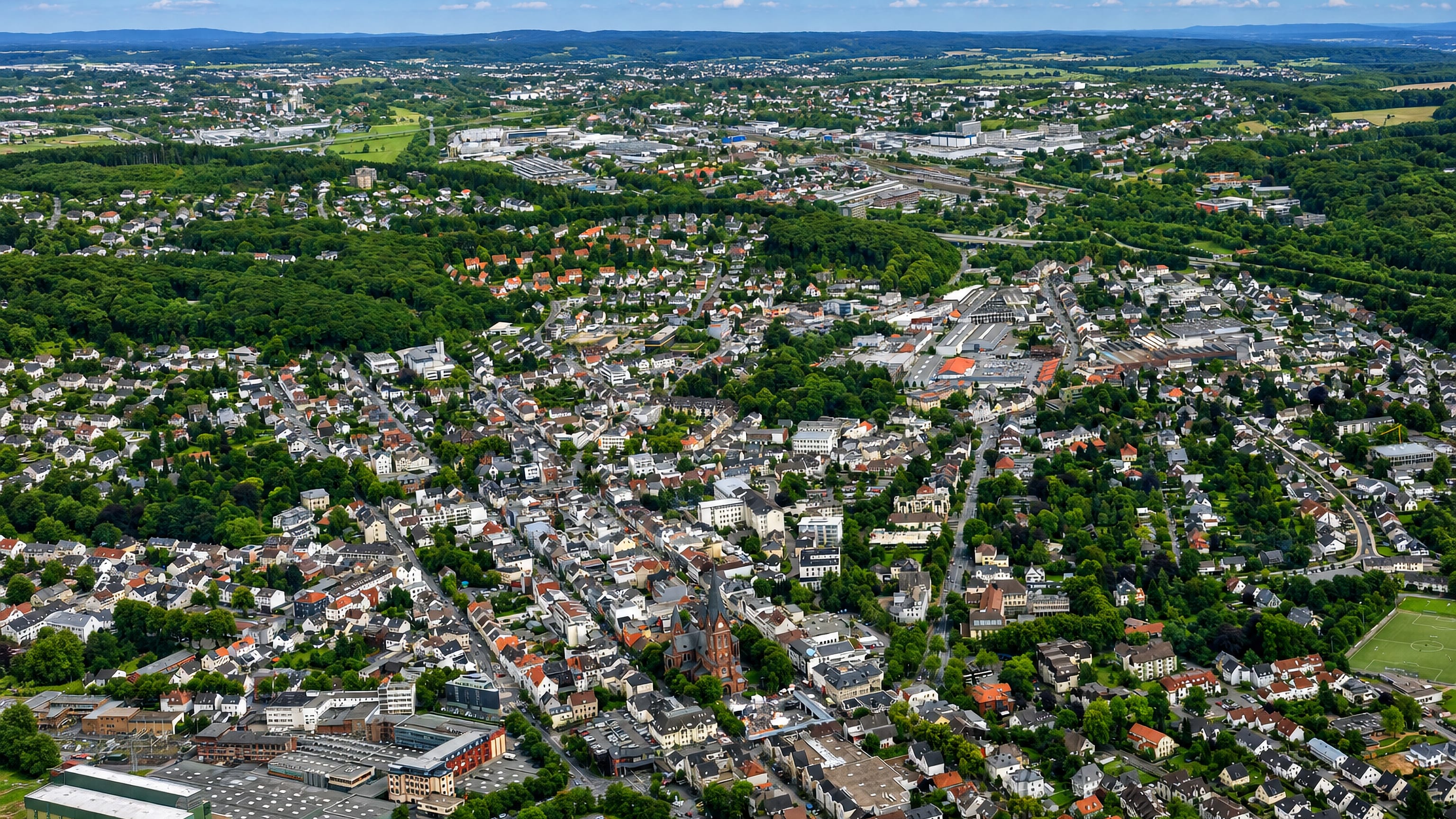 Aerial view of Neheim in Arnsberg, its church tower and dense streets ringed by the wooded hills of the Sauerland