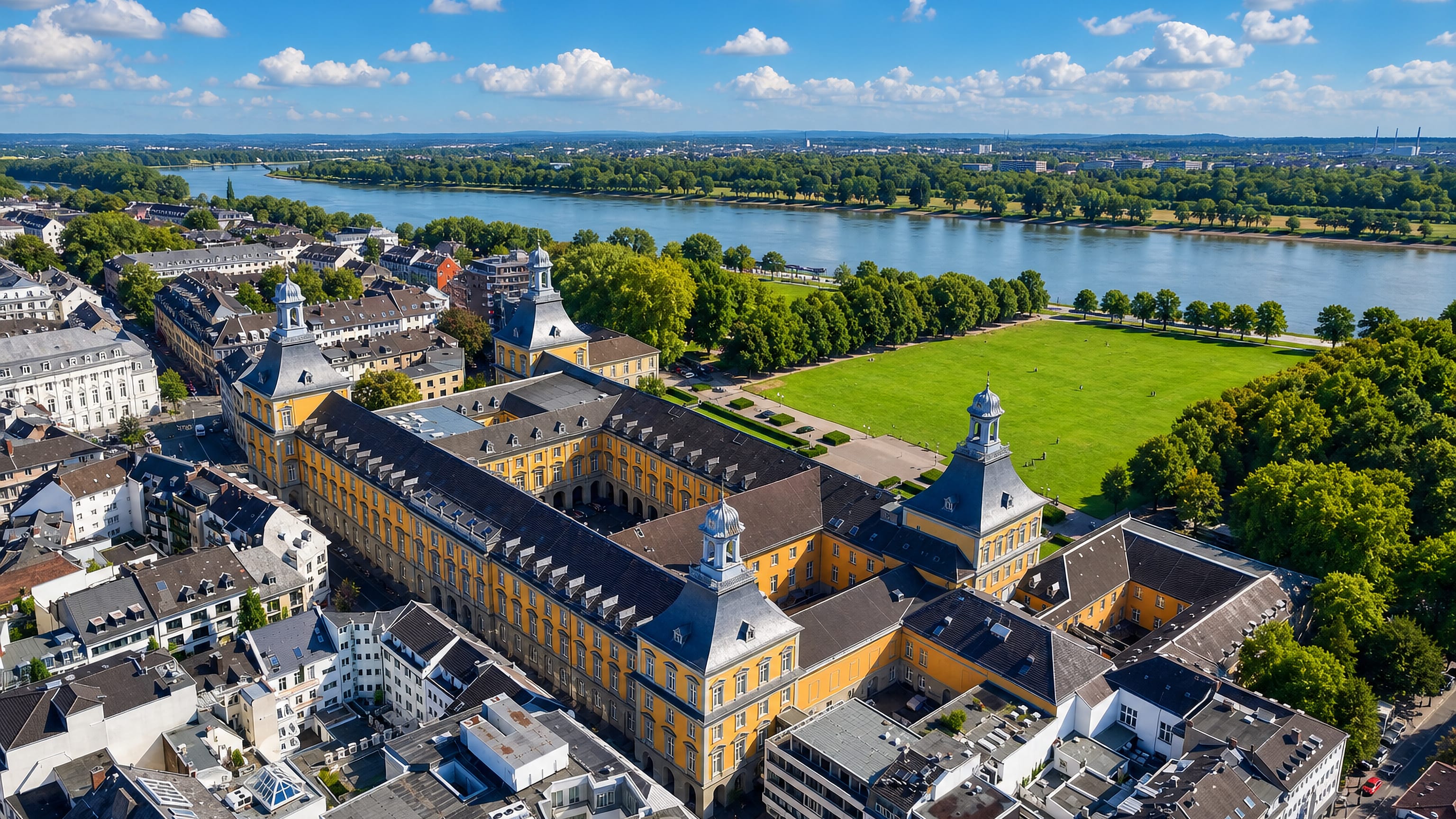 Aerial view of Bonn's yellow Baroque Kurfürstliches Schloss and the Hofgarten lawn with the Rhine beyond