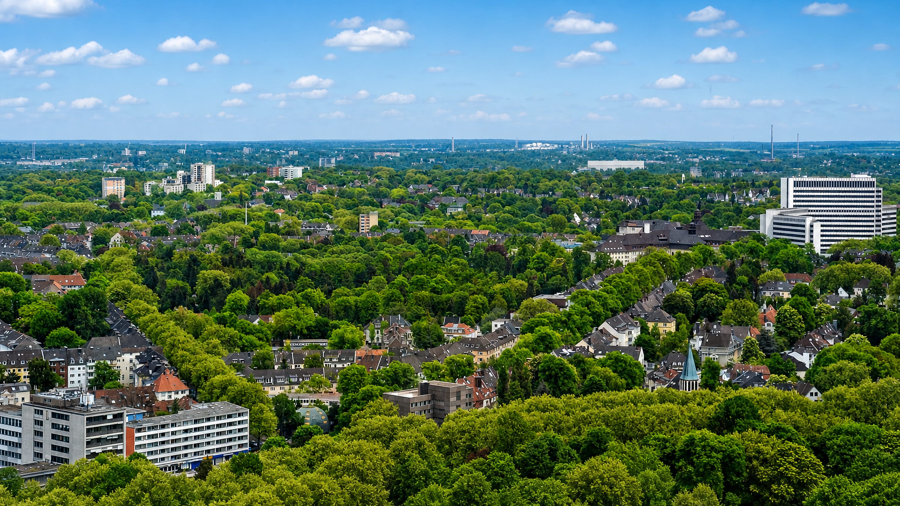 Elevated view over the leafy rooftops of Huttrop in Essen, with office towers and Ruhr chimneys beyond