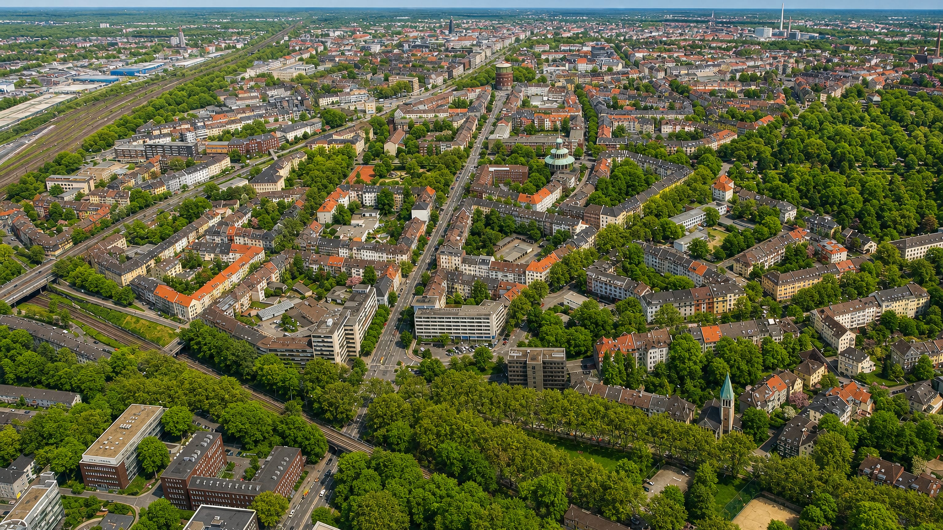 Aerial view over Essen's Südostviertel, with dense red-roofed blocks, rail lines and green boulevards.