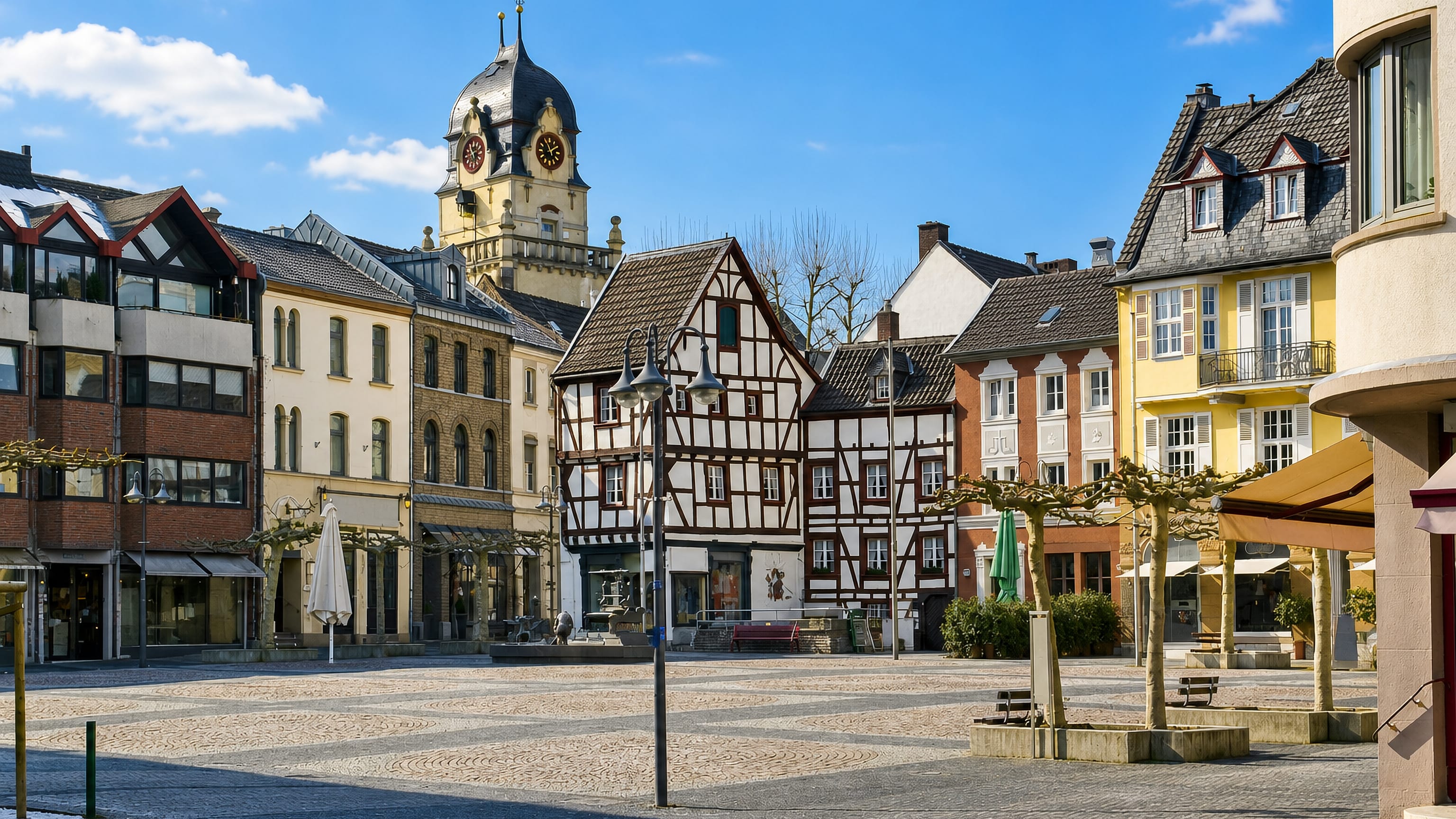 Euskirchen's cobbled market square in Germany, half-timbered houses and a clock-tower spire under blue sky.