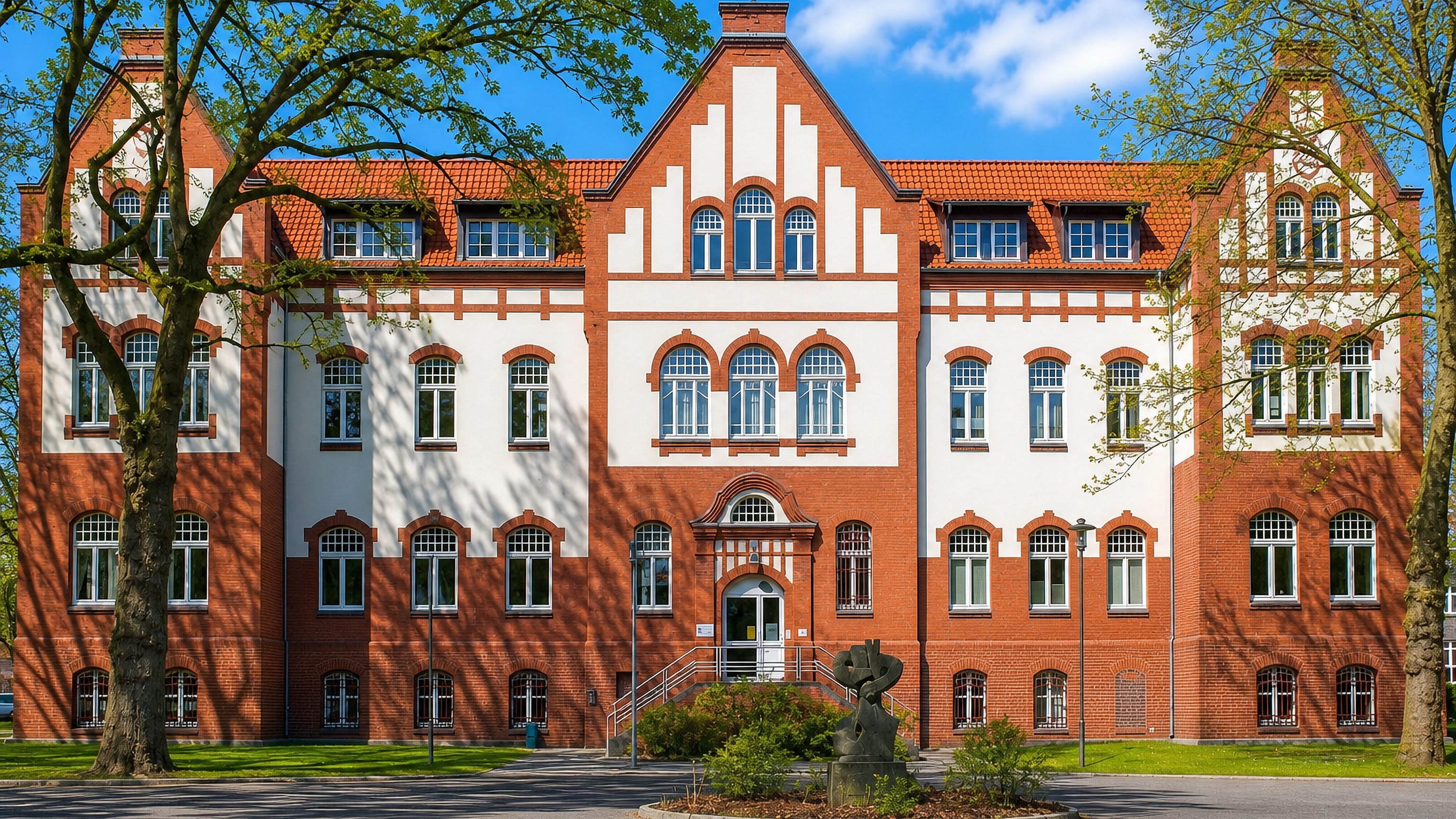 Red-brick gabled civic building framed by trees on a quiet street in Gladbeck, North Rhine-Westphalia.