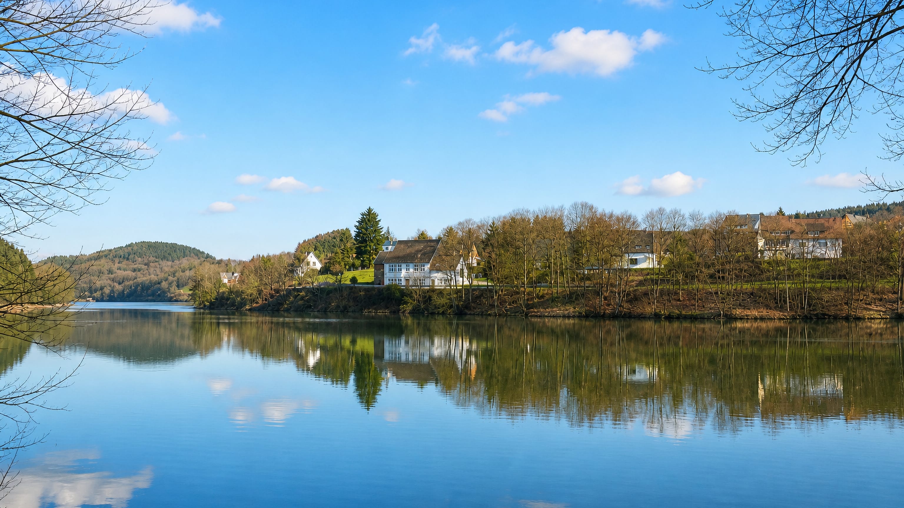 A calm wooded reservoir with a few white houses on the shore near Gummersbach, Germany.