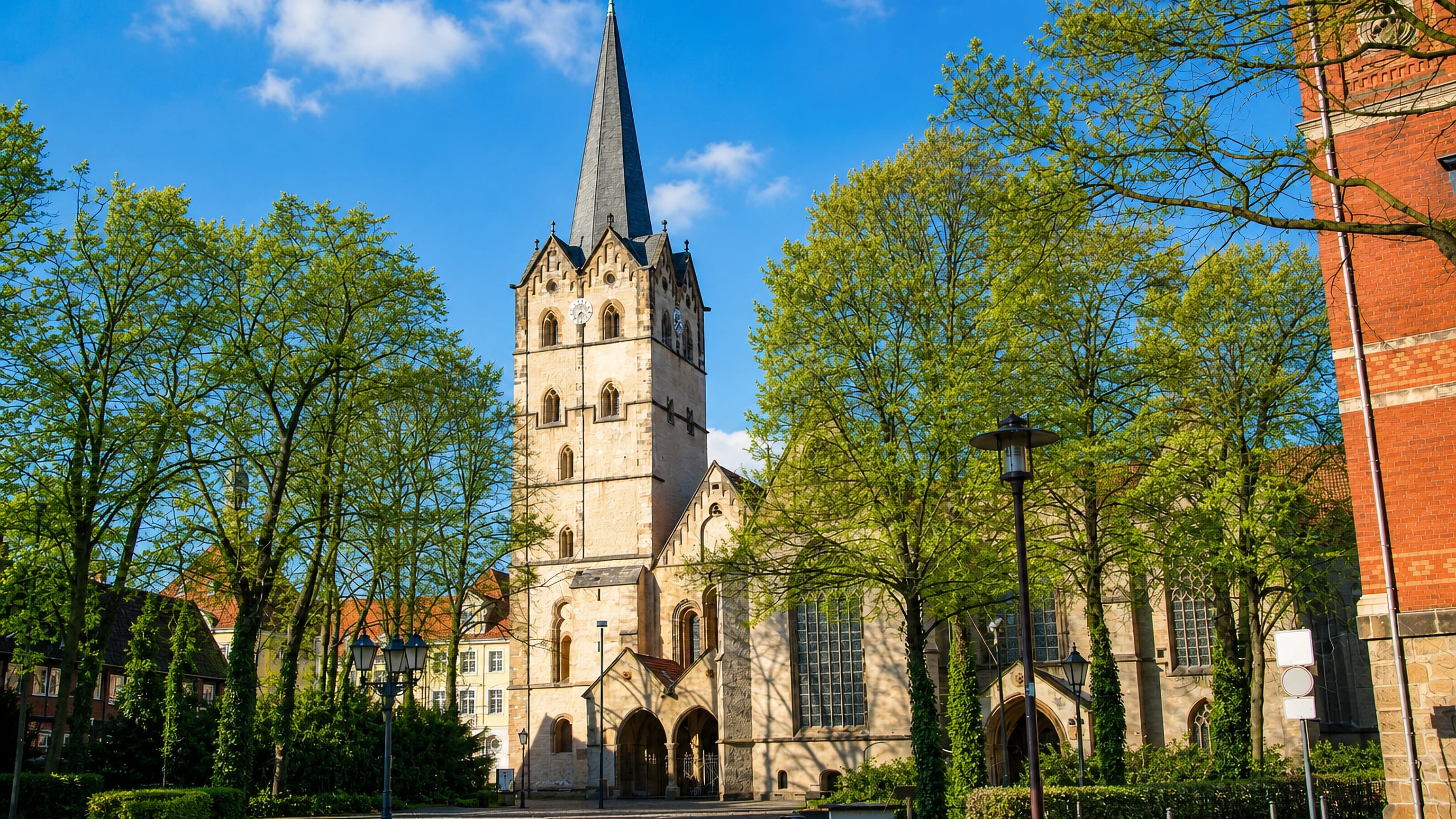 The stone tower and slate spire of Herford Minster rising over a tree-lined cobbled square in Westphalia