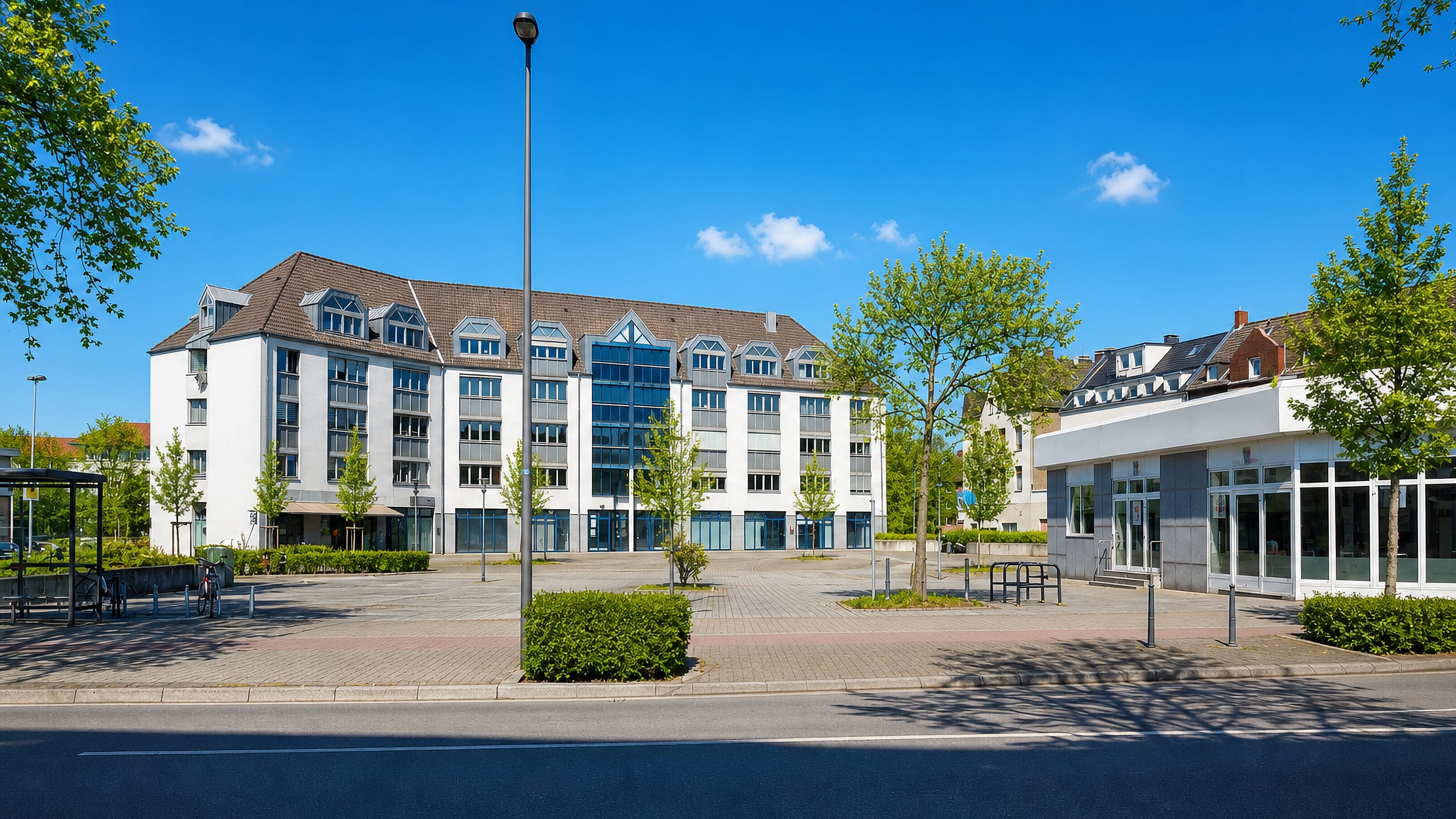 A modern white apartment block and empty paved square beside the main road in Röhlinghausen, Herne.
