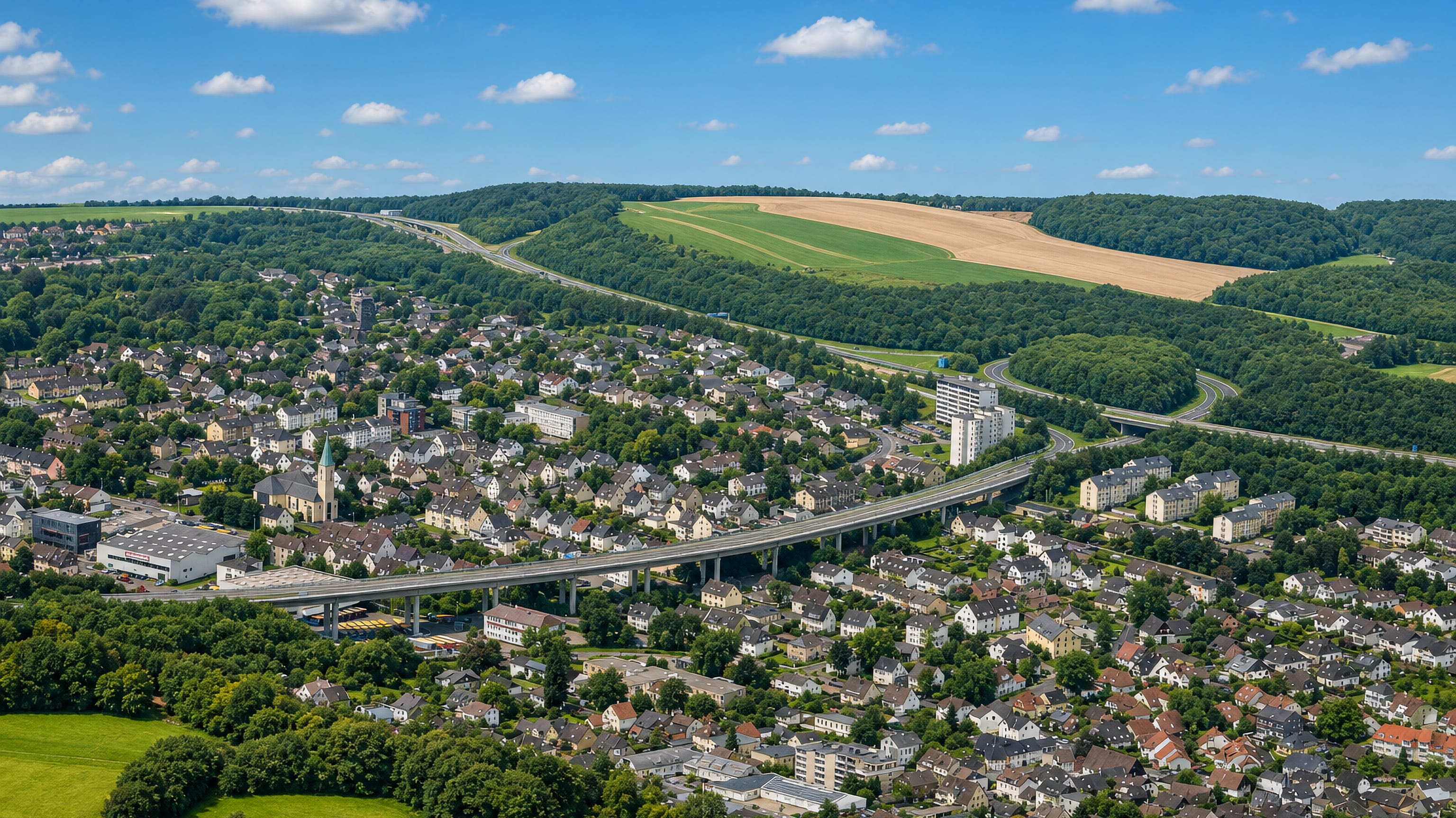 Aerial view of Oestrich in Iserlohn, with a motorway viaduct sweeping past rooftops and wooded hills.
