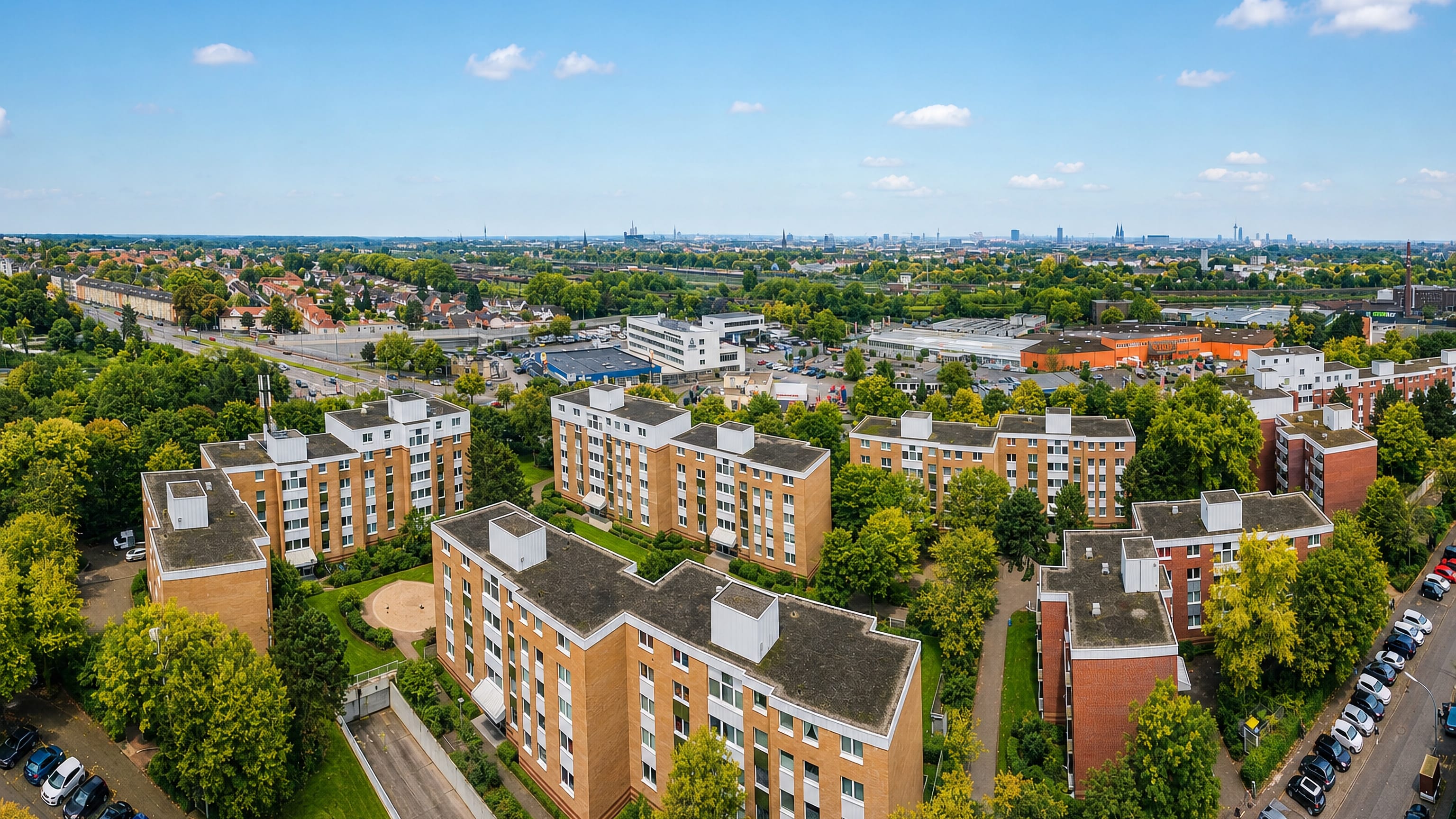 Aerial view over brick apartment blocks in Buchheim, Cologne, with the city's cathedral spires on the horizon.