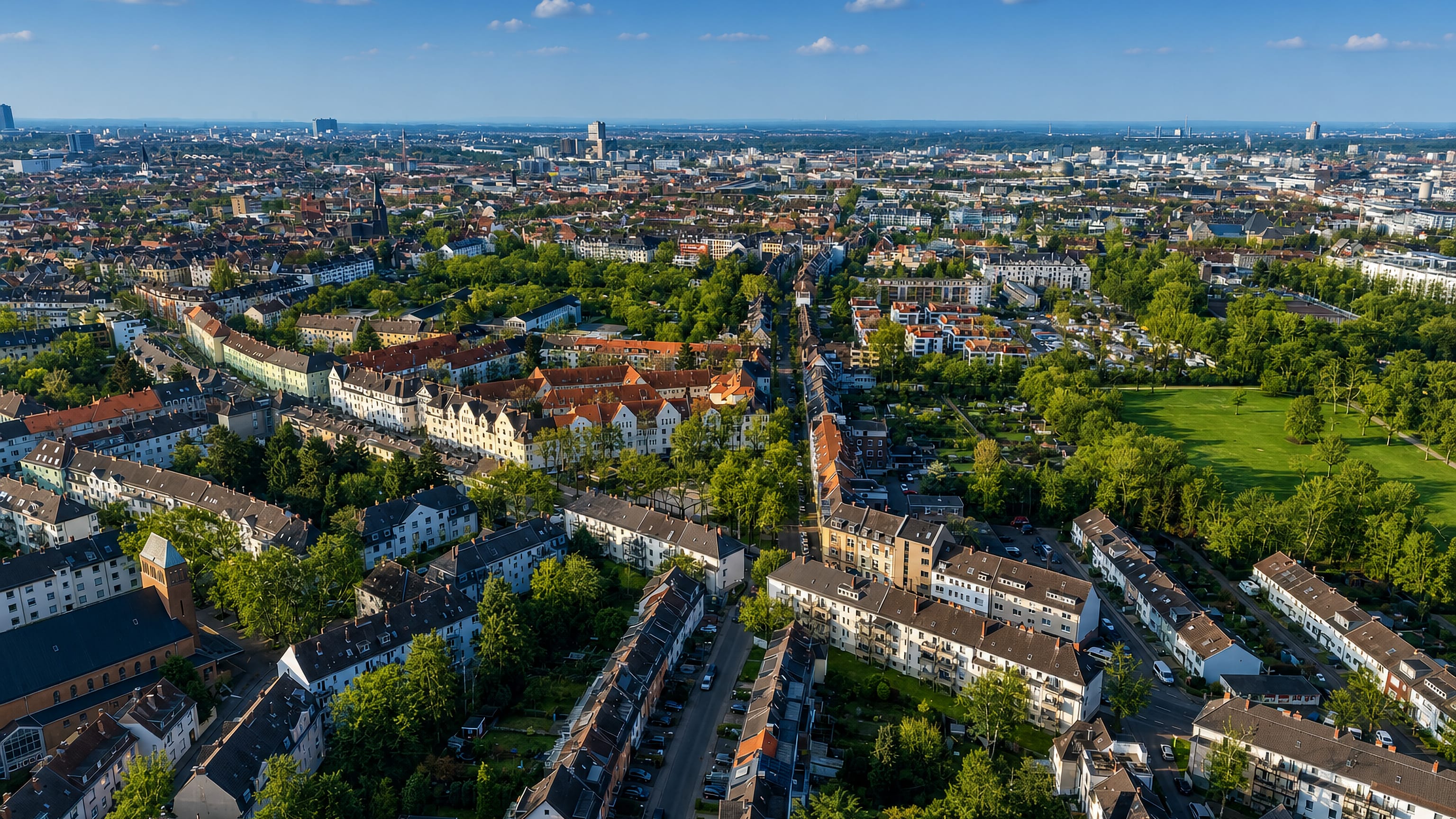 Aerial view over red-roofed residential blocks, allotment gardens and parkland in Neuehrenfeld, Cologne.