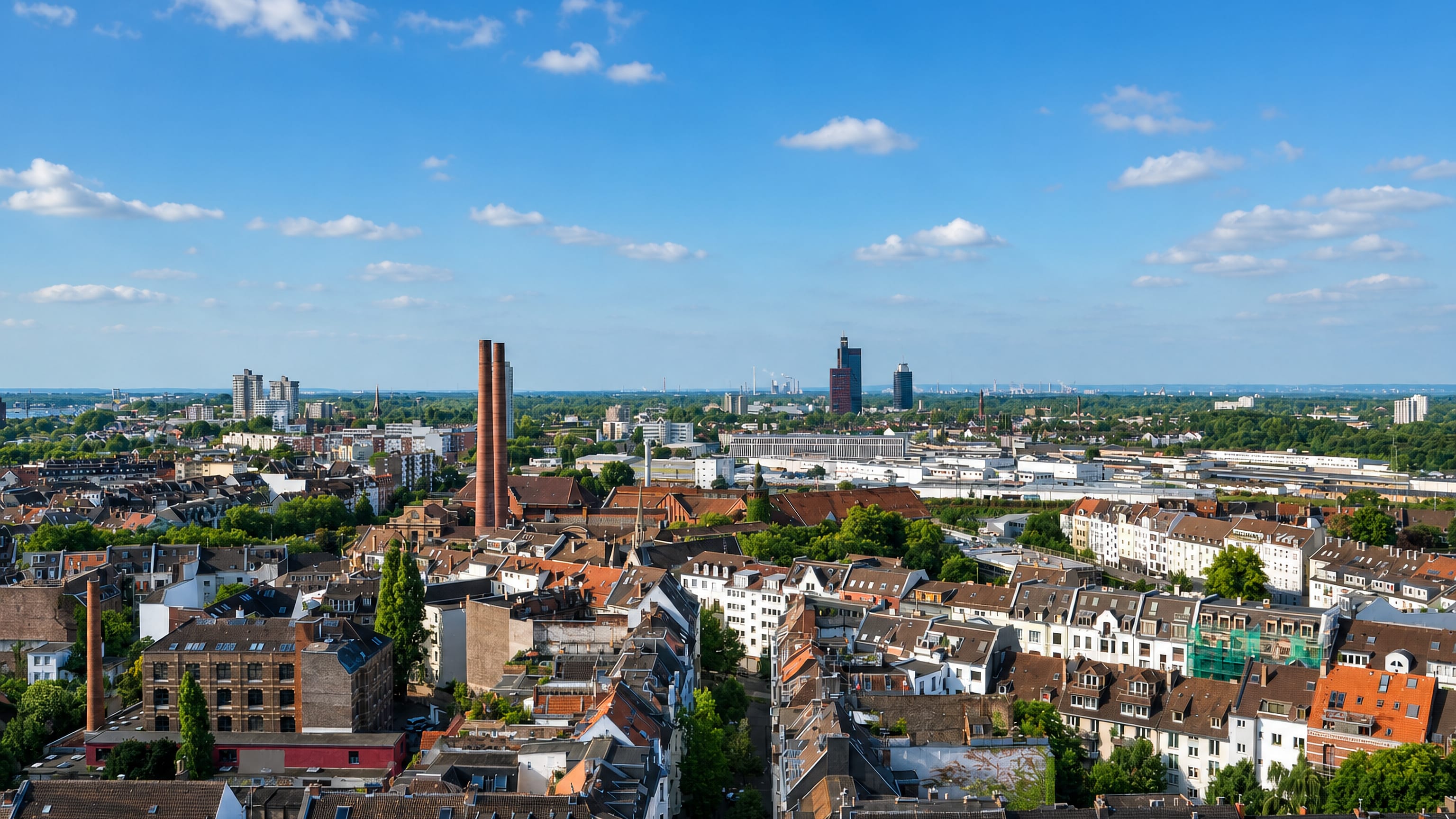 Rooftops, brick chimneys and distant towers across Neustadt/Süd, Cologne, seen from above on a clear day.
