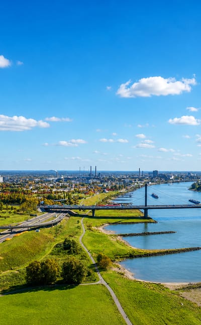 The Rhine curves past green banks toward Leverkusen's distant industrial chimneys.