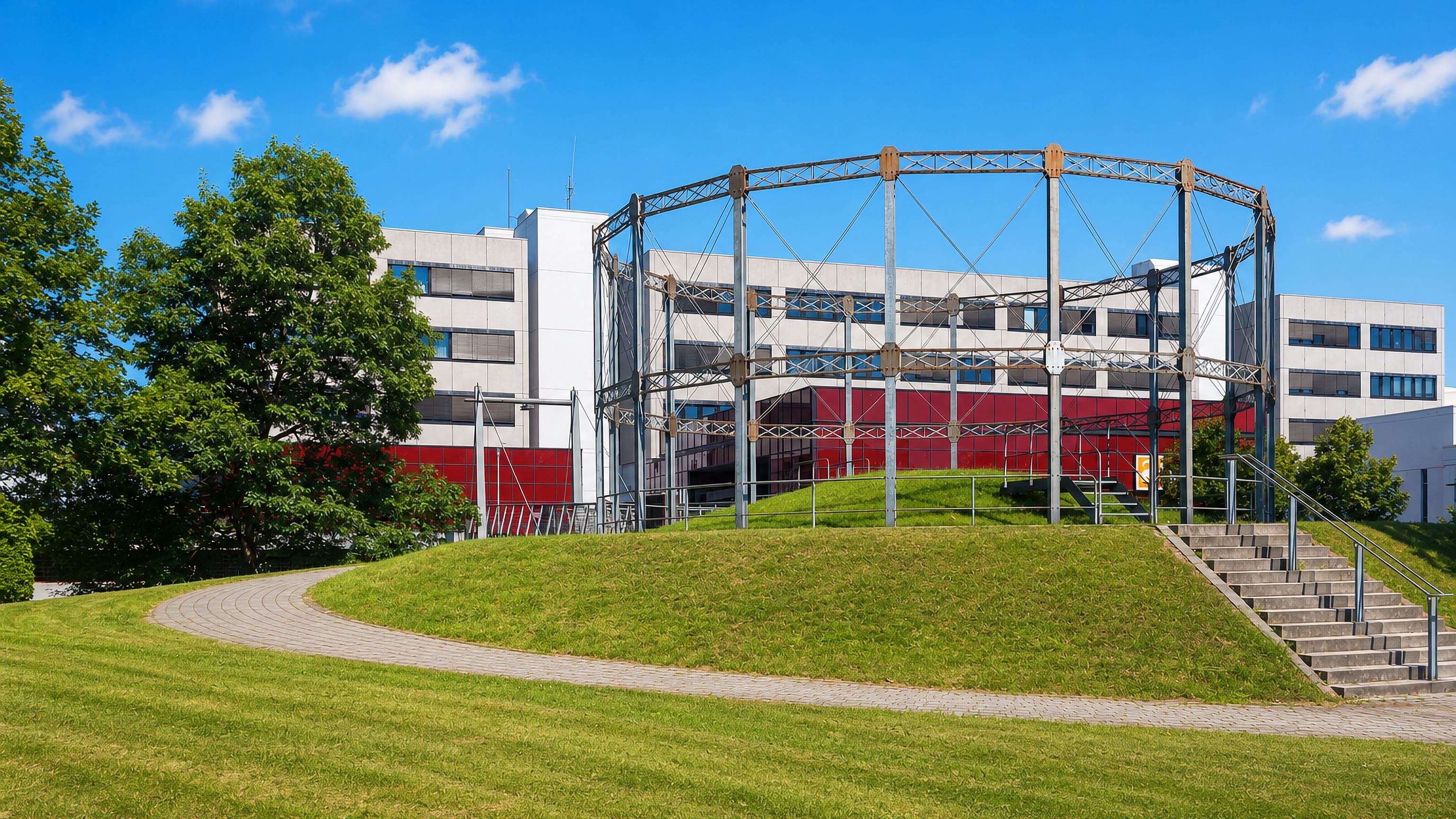 A steel gasholder frame standing on a lawn before a white modernist building in Marl, Germany.