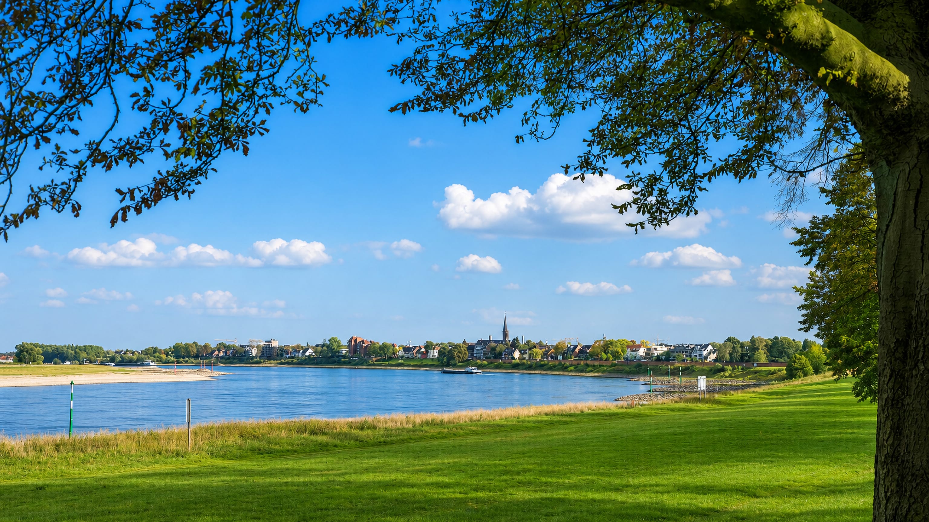 The Rhine at Grimlinghausen, Neuss, with riverside meadows and the village skyline and church spire beyond