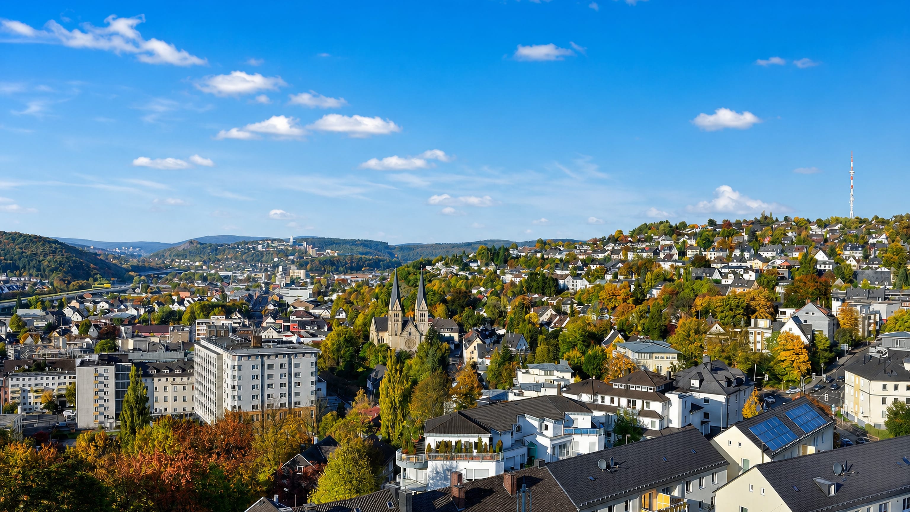 Siegen, North Rhine-Westphalia, in autumn with a twin-spired church, hillside houses and wooded Siegerland hills.
