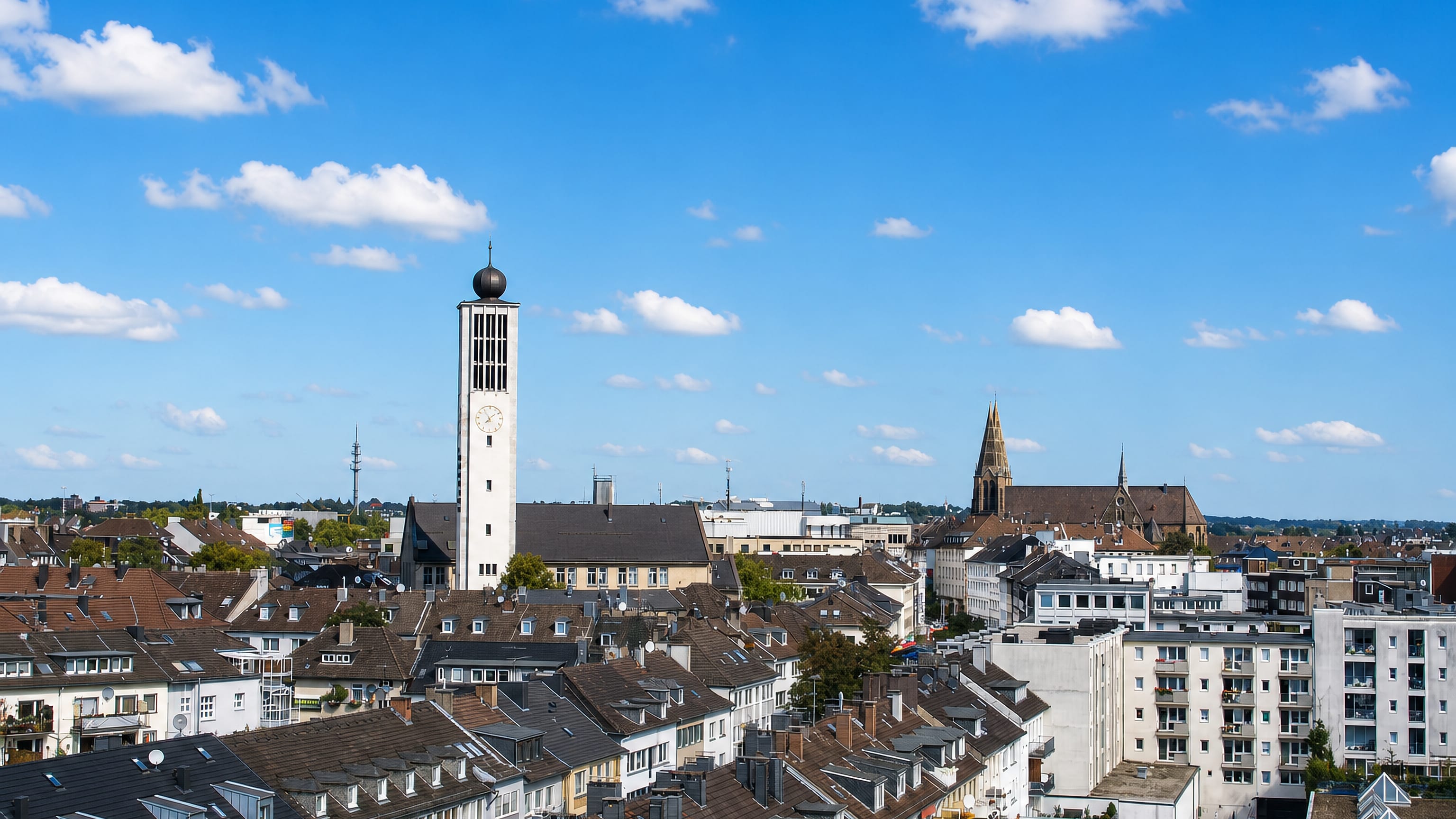 Sunlit rooftops of central Solingen, Germany, with a tall white church bell tower and a neo-Gothic spire beyond.