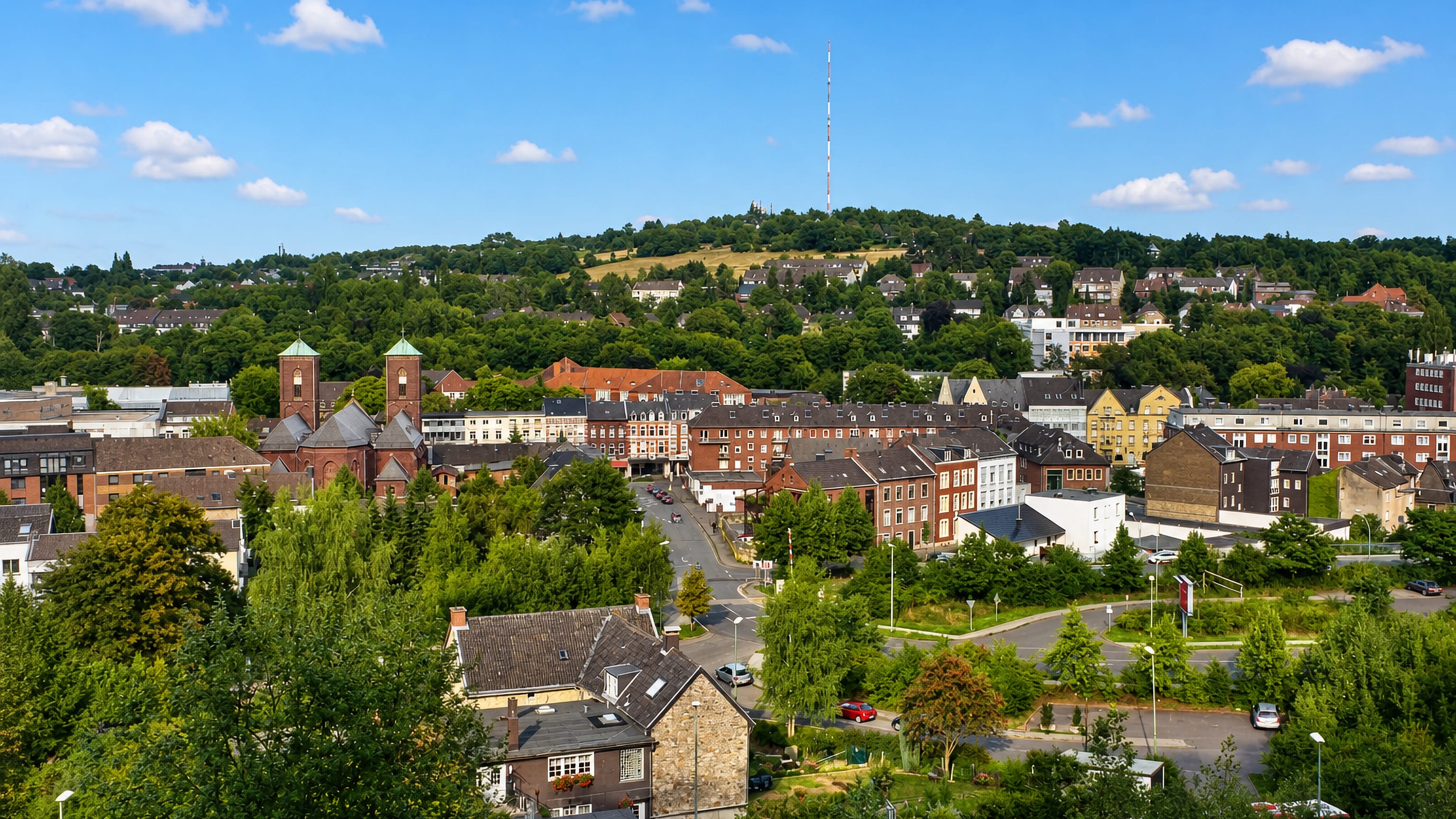 Townscape of Donnerberg in Stolberg, with a twin-towered brick church and a transmitter mast on the wooded hill.