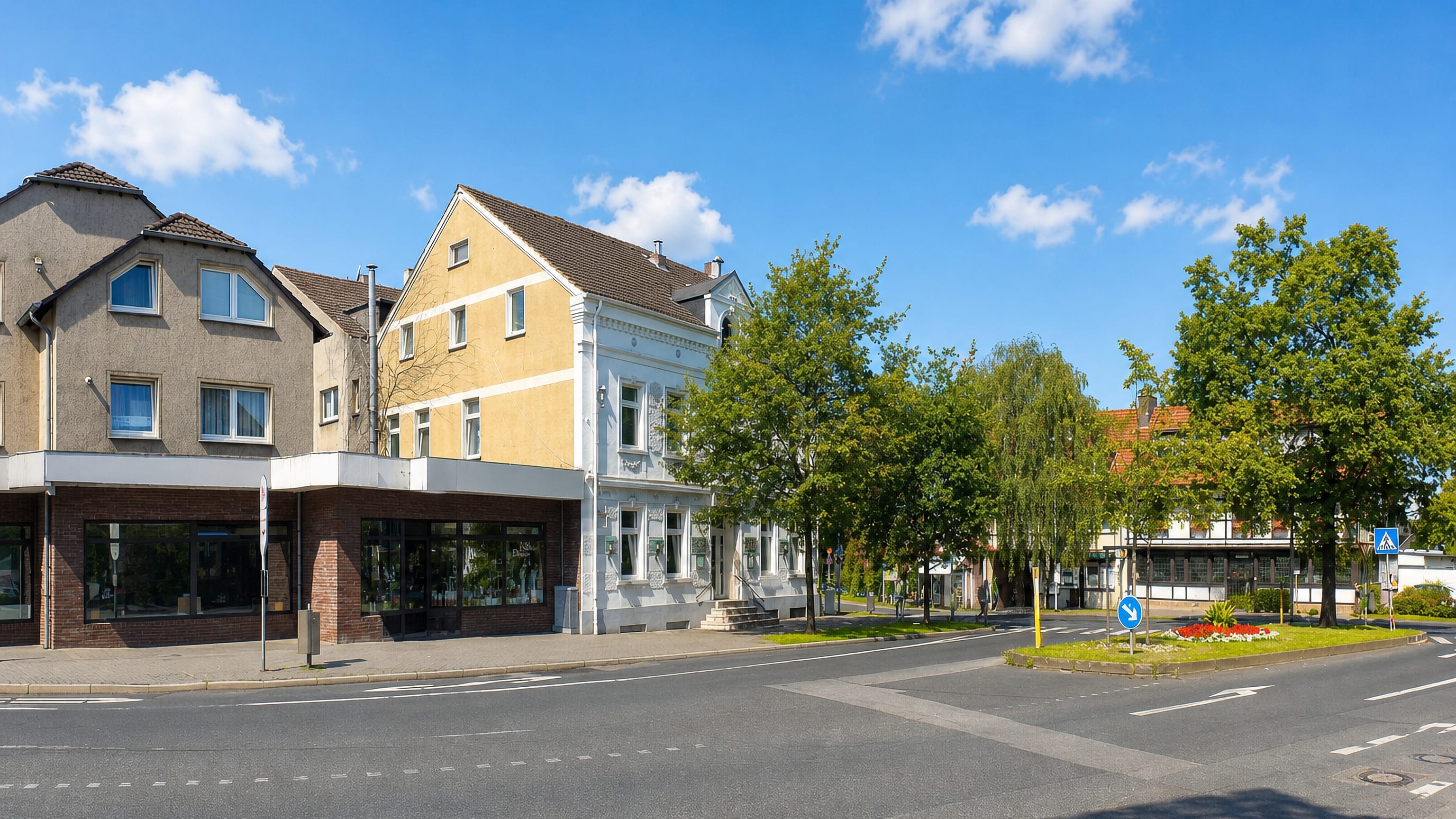 Sunlit street corner in Eppendorf, Wattenscheid, with gabled shop-fronted houses and leafy trees under a blue sky
