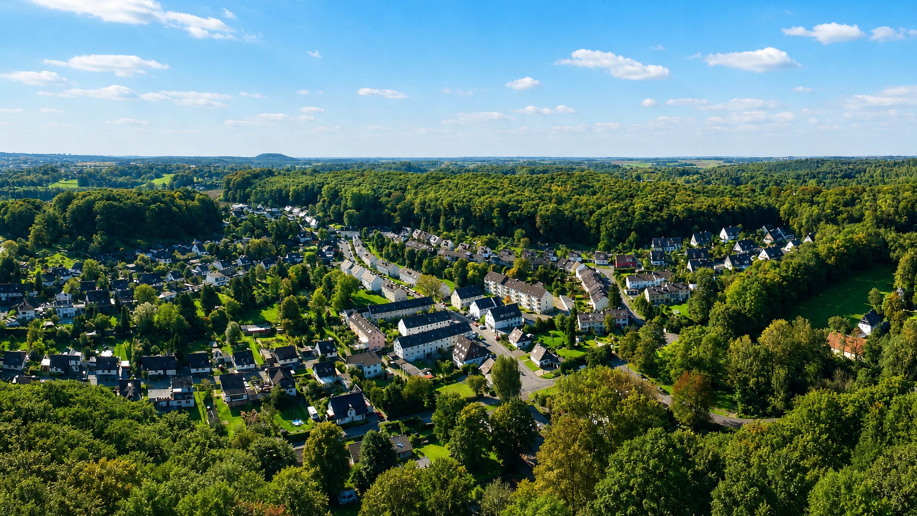 Aerial view over the wooded suburb of Lüntenbeck in Wuppertal, with detached houses set among green woodland.