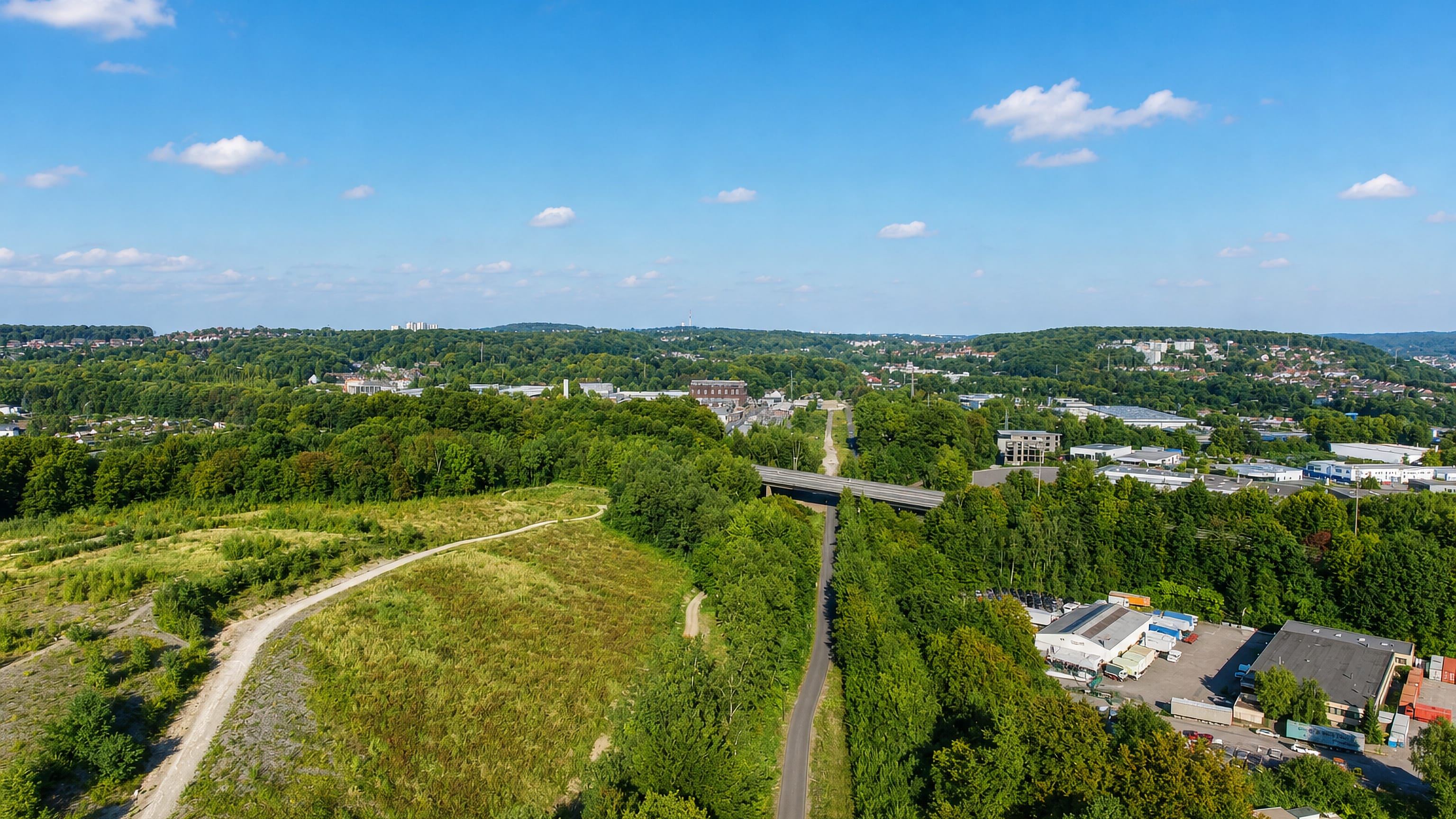 Aerial view across wooded hills, a valley road and light industry at Nützenberg, Wuppertal.