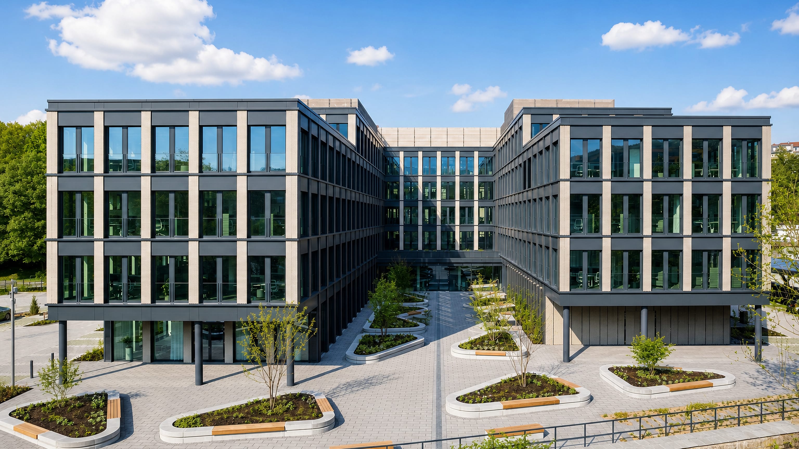 Modern grey office complex around a landscaped courtyard in Rauental, Wuppertal, under a clear blue sky.