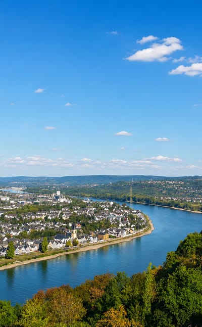 A town spread along a bend of the Rhine river with wooded hills beyond, near Koblenz, Germany.