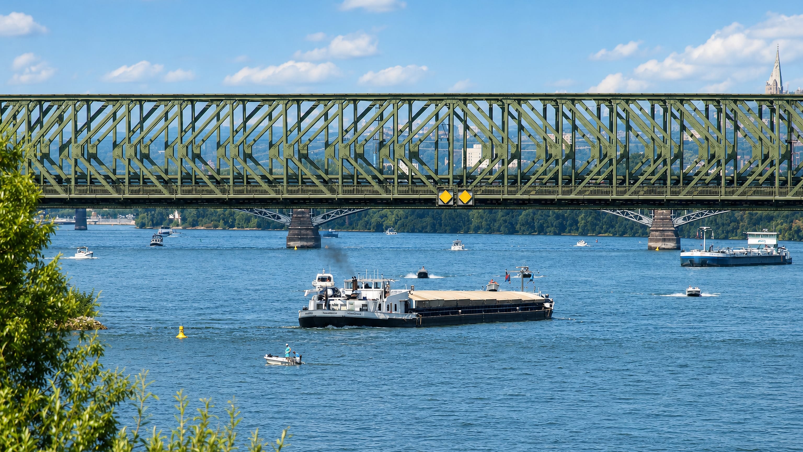 The green steel Südbrücke railway bridge spanning the Rhine at Weisenau, Mainz, with a cargo barge passing.