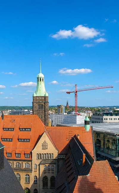Rooftop view over Chemnitz with green-copper church spires, red-tiled roofs and a distant high-rise.