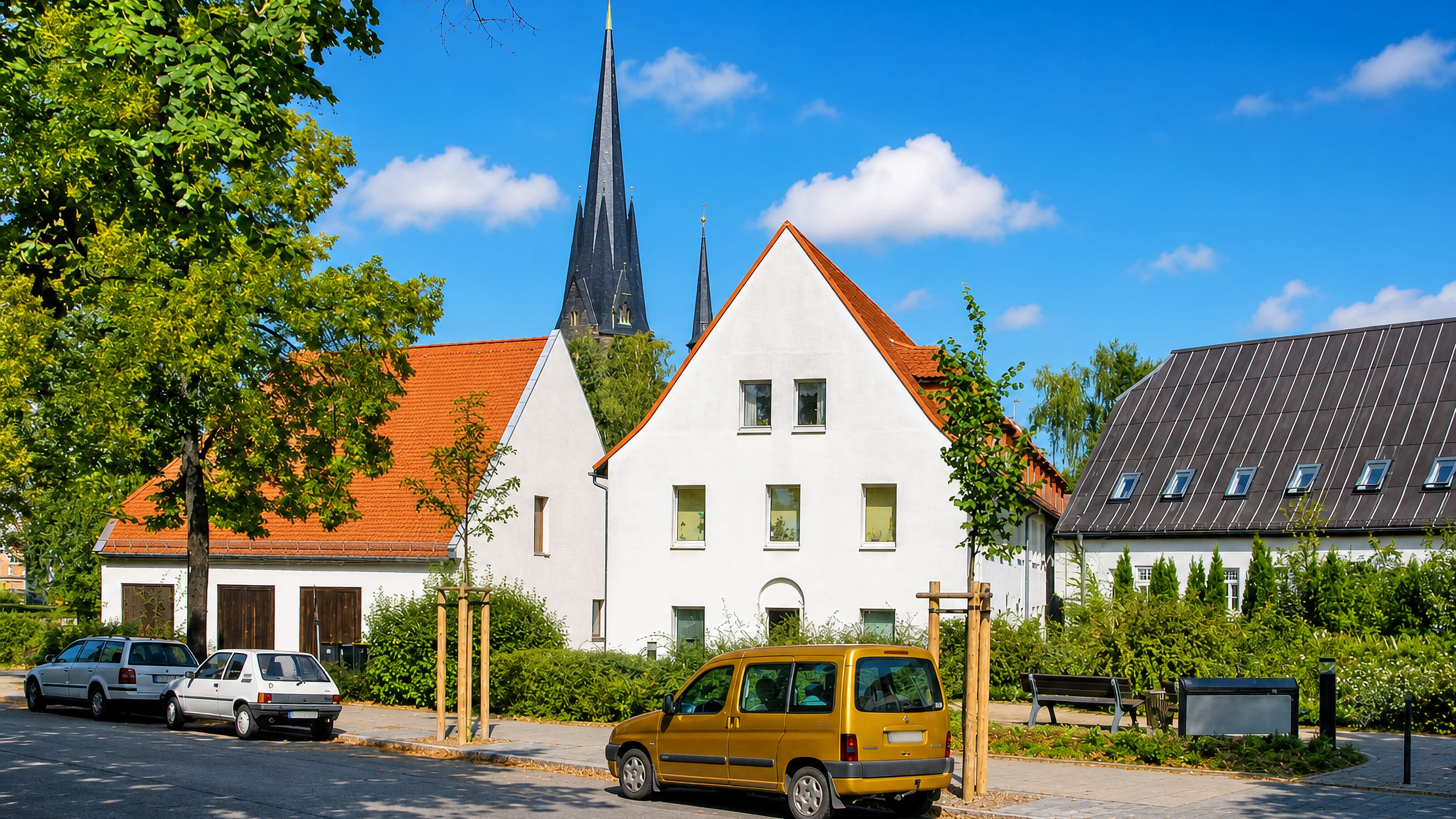 White gabled houses and a dark church spire above a quiet residential street in Leuben, Dresden.