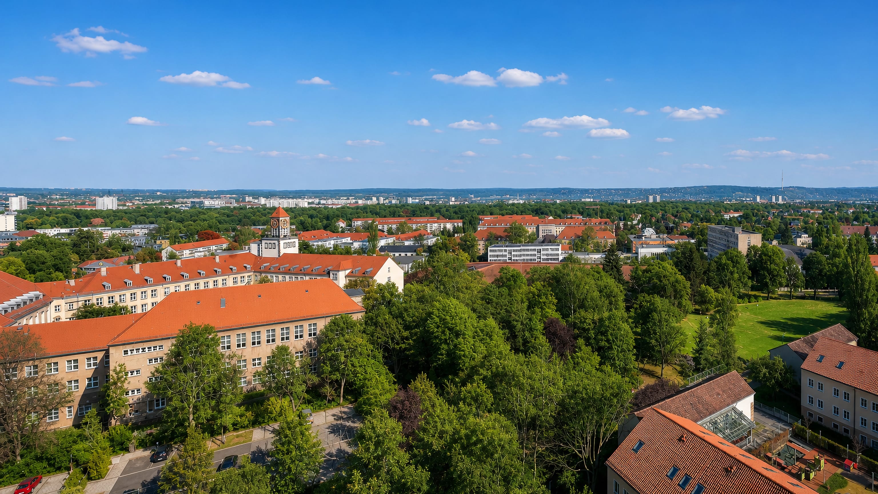 Red-tiled roofs and a clock-towered brick complex among trees in Strehlen, Dresden.